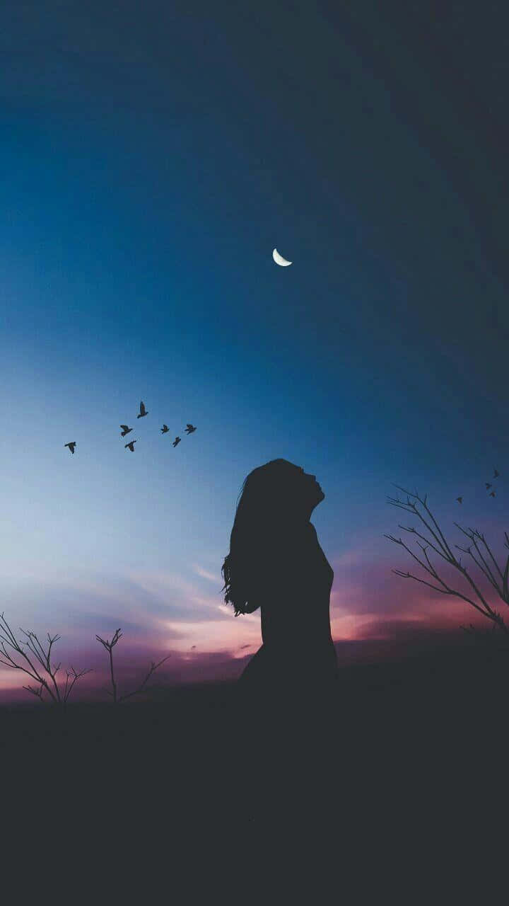 剪影中的女人在暮色中仰望月亮和飛鳥。