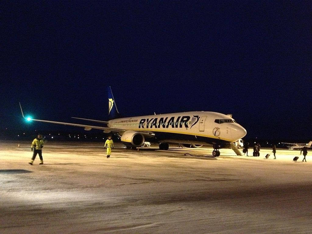 夜間積雪跑道上的瑞安航空飛機，地勤人員在附近行走。
