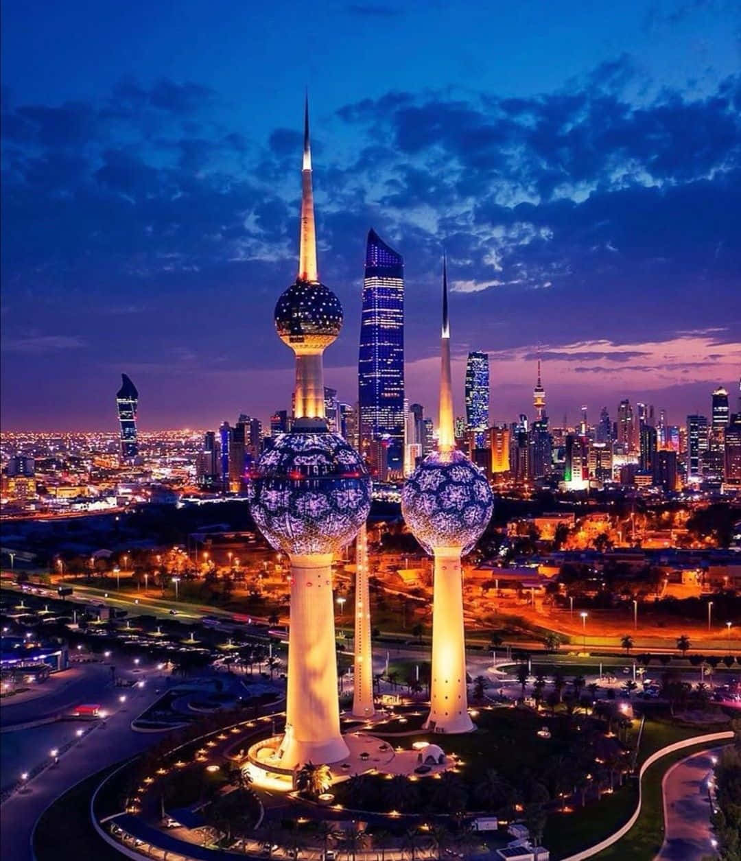 夜間科威特塔手機壁紙 壁紙 — 三座亮燈的科威特塔在暮色天空中閃耀，映襯著廣闊的城市景觀和發光的摩天大樓。