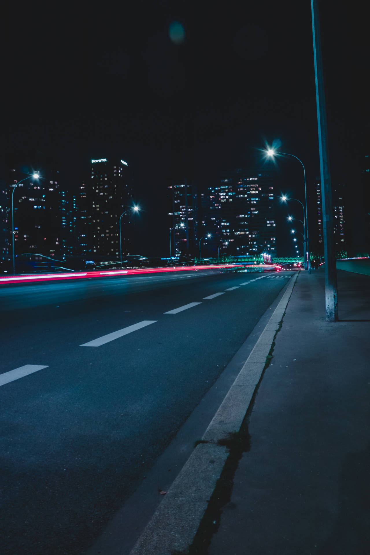 夜間城市街道，有移動車輛的紅色光軌和照明建築。