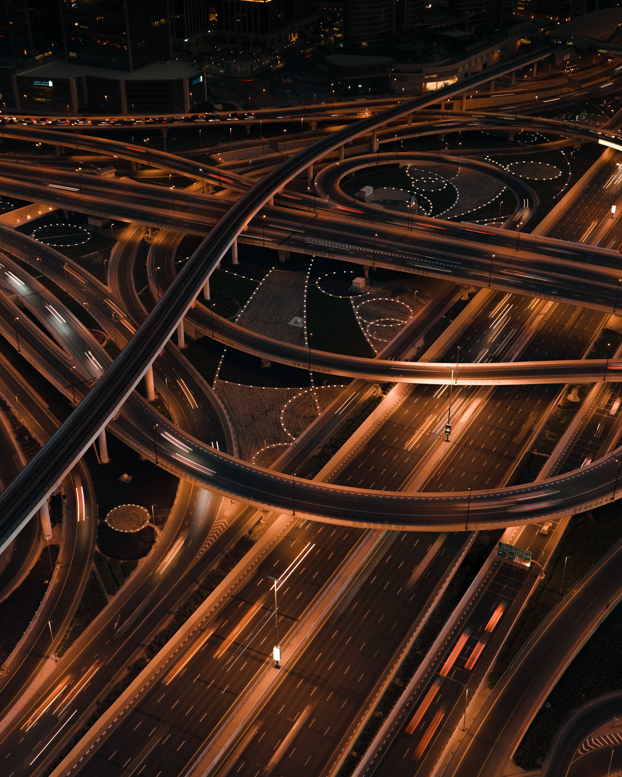 夜間繁忙高速公路交匯處：令人困惑的背景 壁紙 — 夜晚發光高速公路交匯處的鳥瞰圖，汽車燈光軌跡蜿蜒穿過彎曲的高架橋。