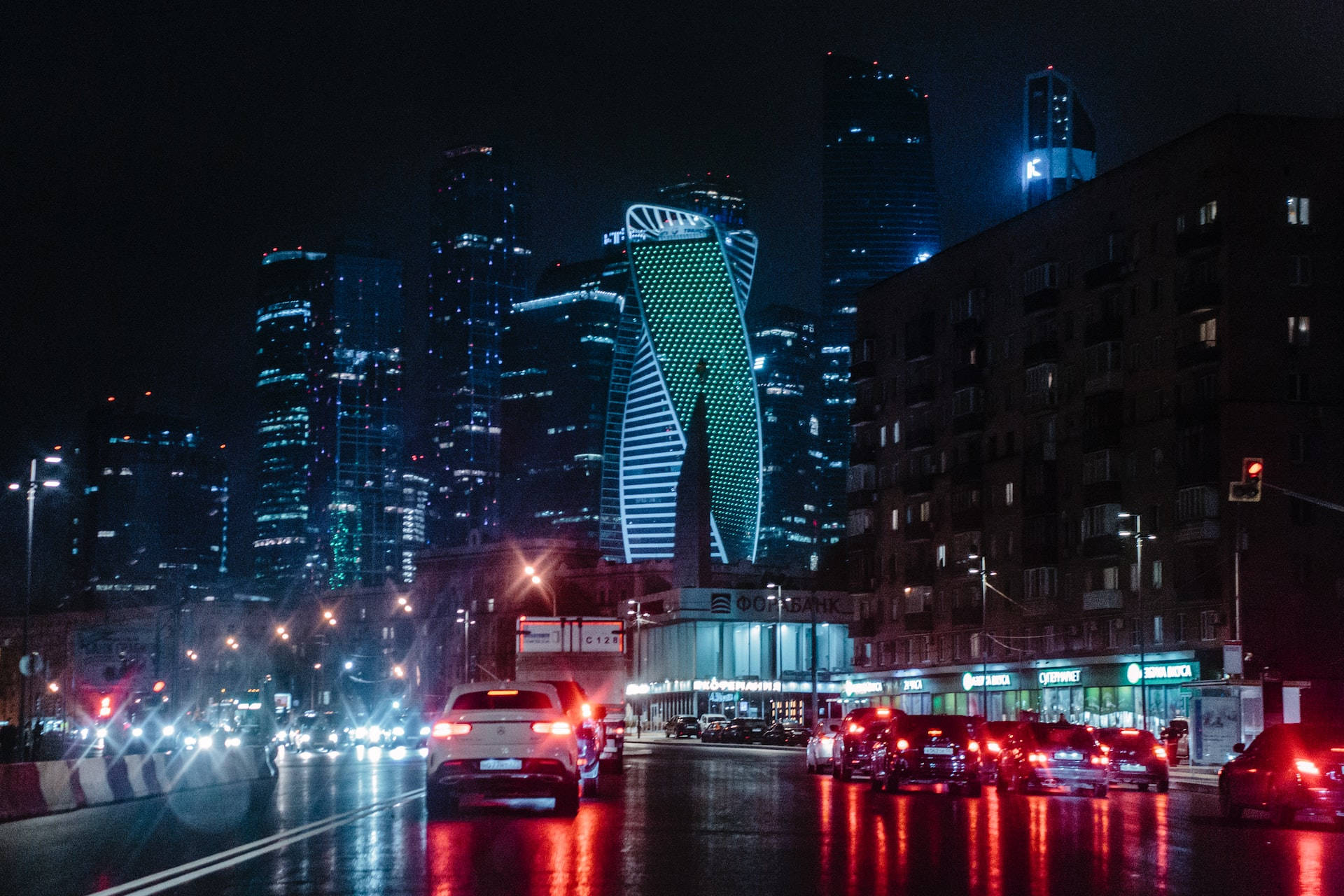夜晚城市街道，發光的建築物和潮濕的人行道反射汽車燈光。