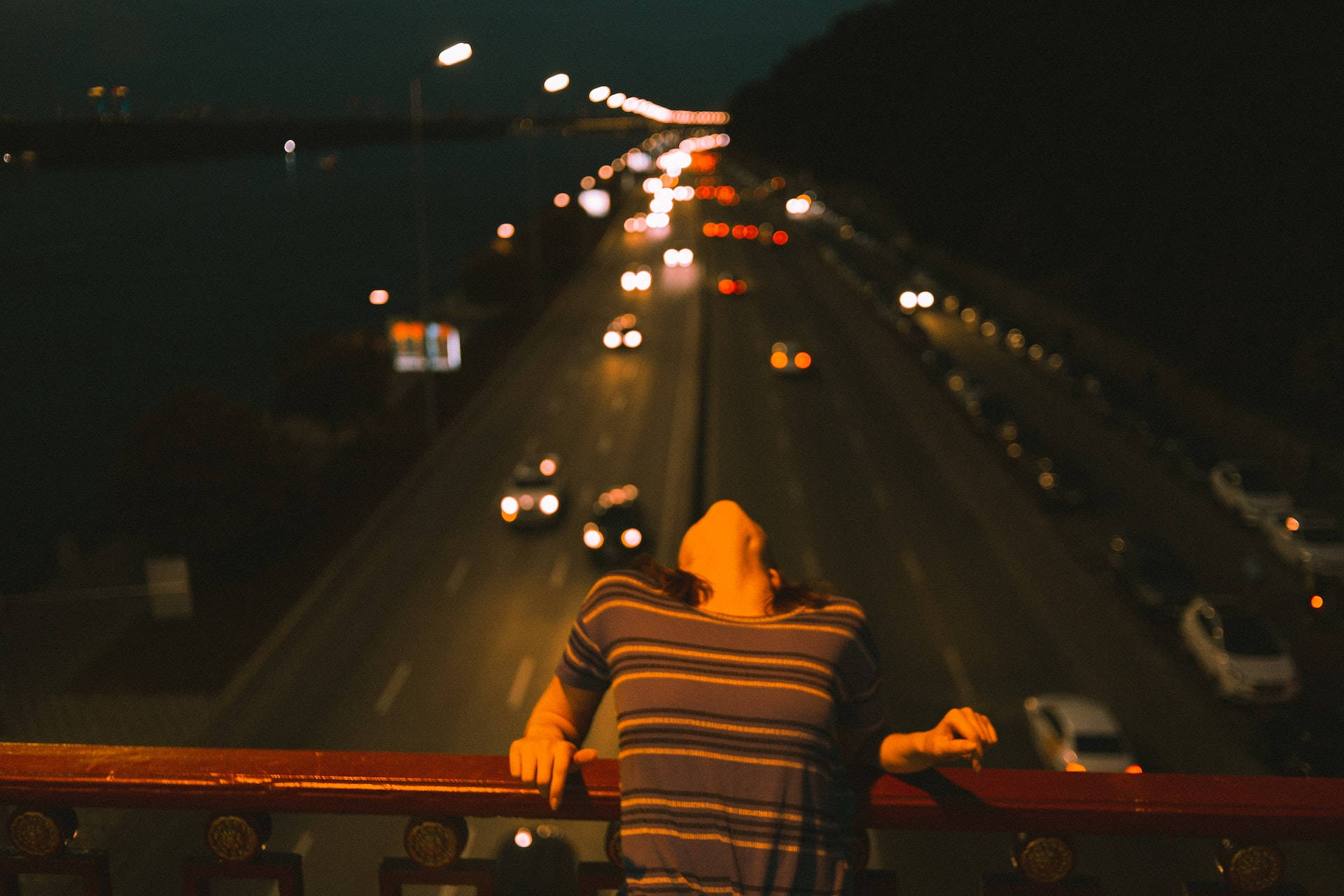 人靠在欄杆上觀看夜晚高速公路上發光的汽車