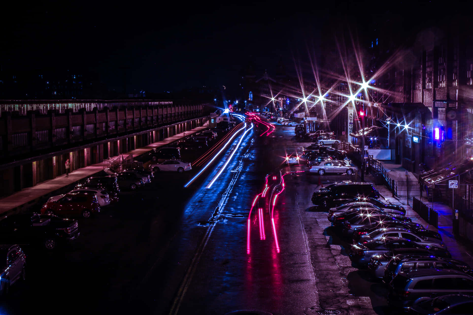 夜間城市街道，在明亮街燈下，有車燈光軌和濕漉漉的路面。