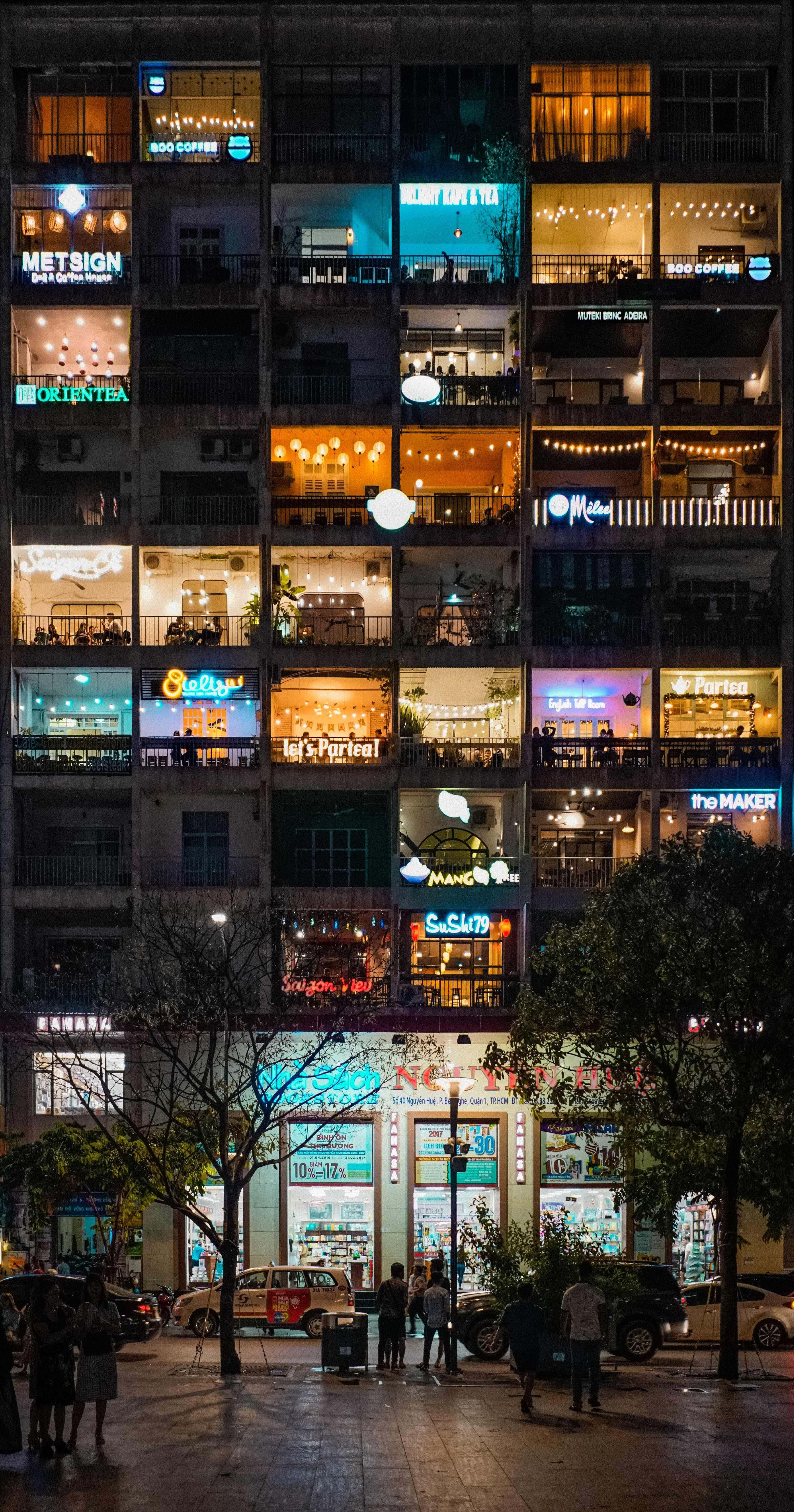夜間迷人咖啡公寓 iPhone 背景 壁紙 — 一座多層建築的充滿活力的夜景，發光的咖啡館和商店櫥窗照亮了下方的城市街道。