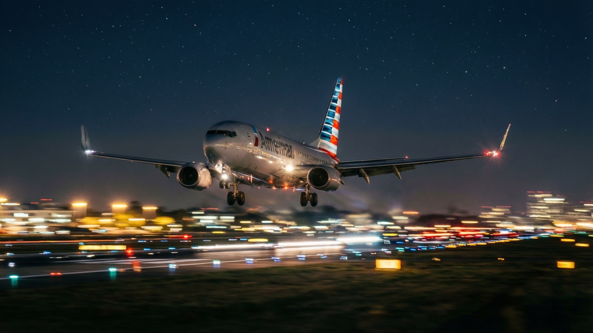 夜間降落 壁紙 — 一架美國航空飛機在夜晚下降，星空和模糊的城市燈光在下方。