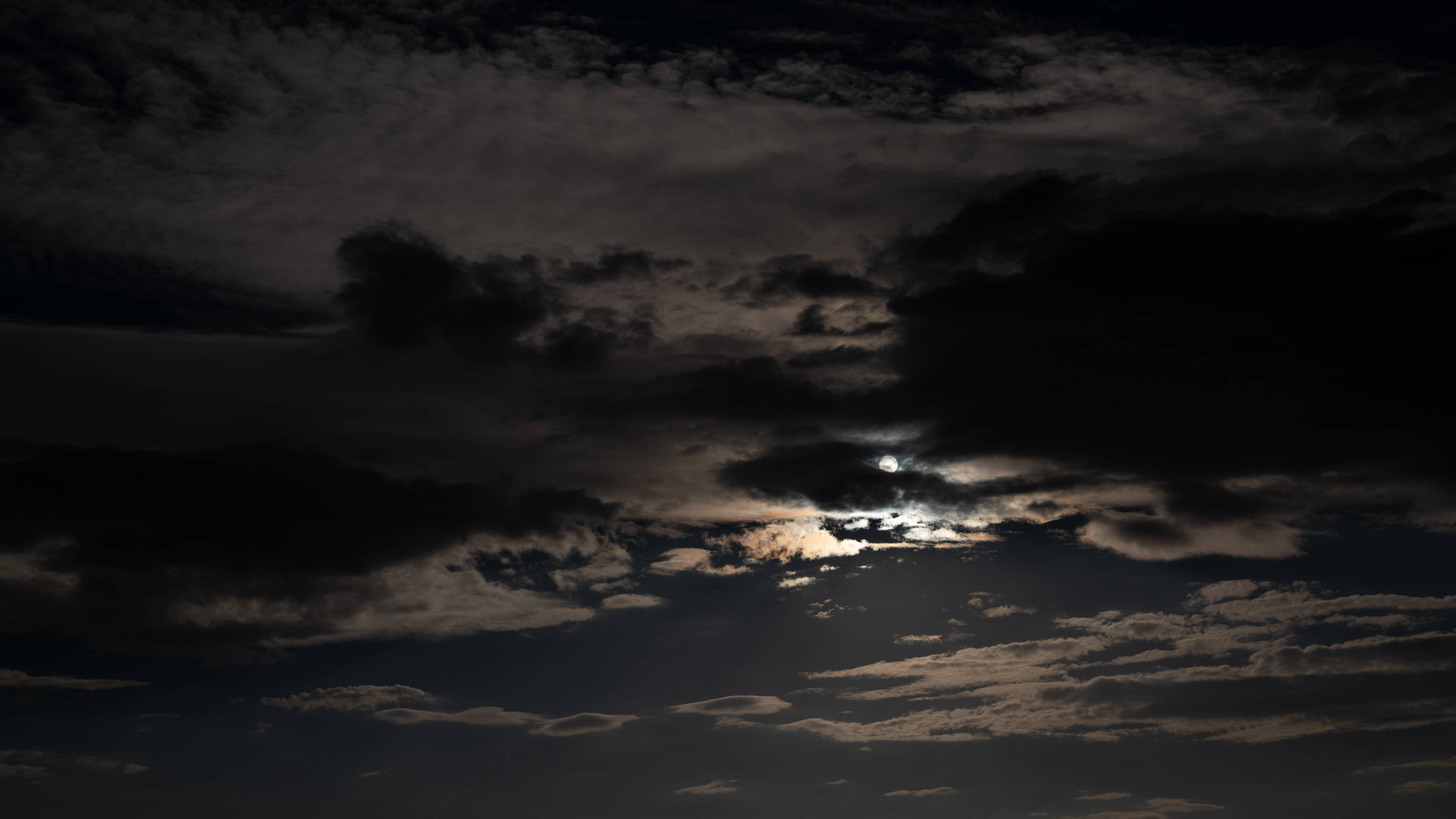 夜間雲層遮月 4K 壁紙 — 一輪明亮的月亮穿透濃密的烏雲，在陰鬱的夜空中灑下空靈的光芒。
