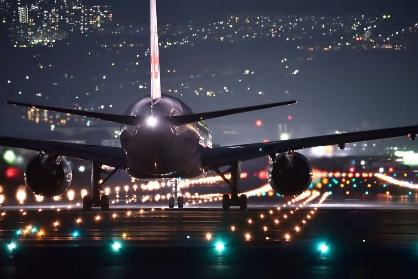 夜間飛機圖像 壁紙 — 一架大型飛機在夜間停在跑道上，背景中城市燈光閃爍。