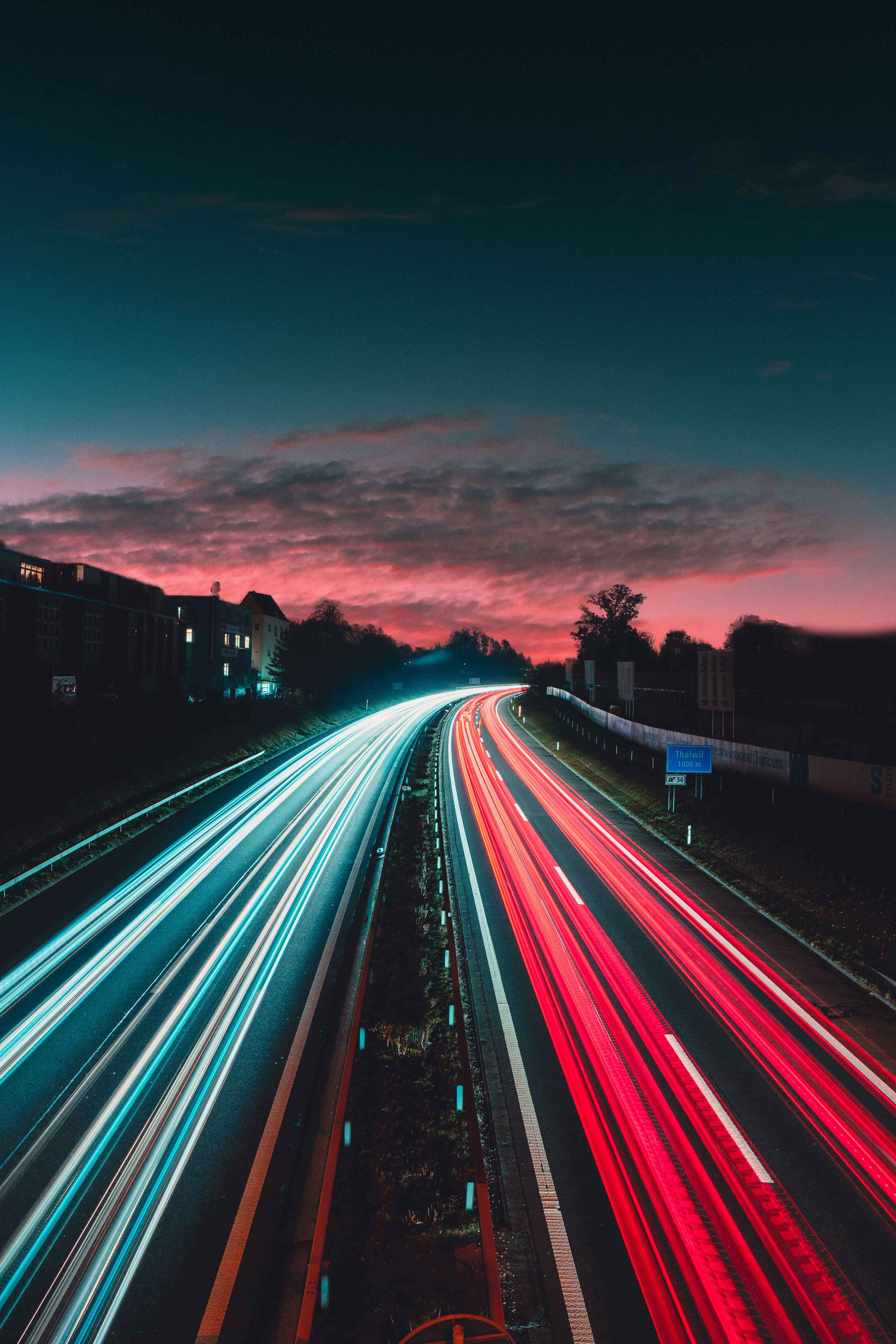 夜間高速公路 iPhone 背景 壁紙 — 長時間曝光捕捉到紅色和藍色車燈在黃昏時分沿高速公路飛馳的光軌。