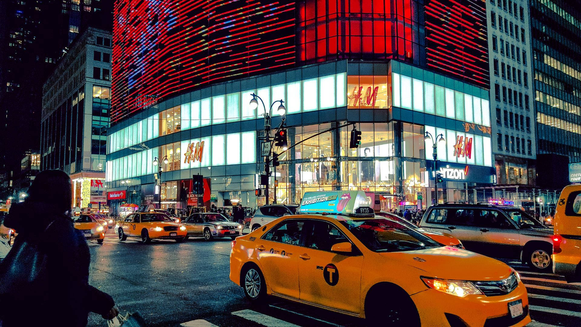 夜間黃色計程車對比H&M商店 壁紙 — 充滿活力的夜景城市景觀，特色是黃色的士和帶有H&M標誌的紅色發光建築。