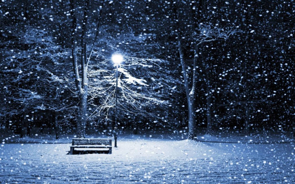 夜雪公園長椅冬季桌面 壁紙 — 一張孤獨的雪覆蓋長椅在路燈下發光，夜晚的寧靜冬季公園中大雪紛飛。