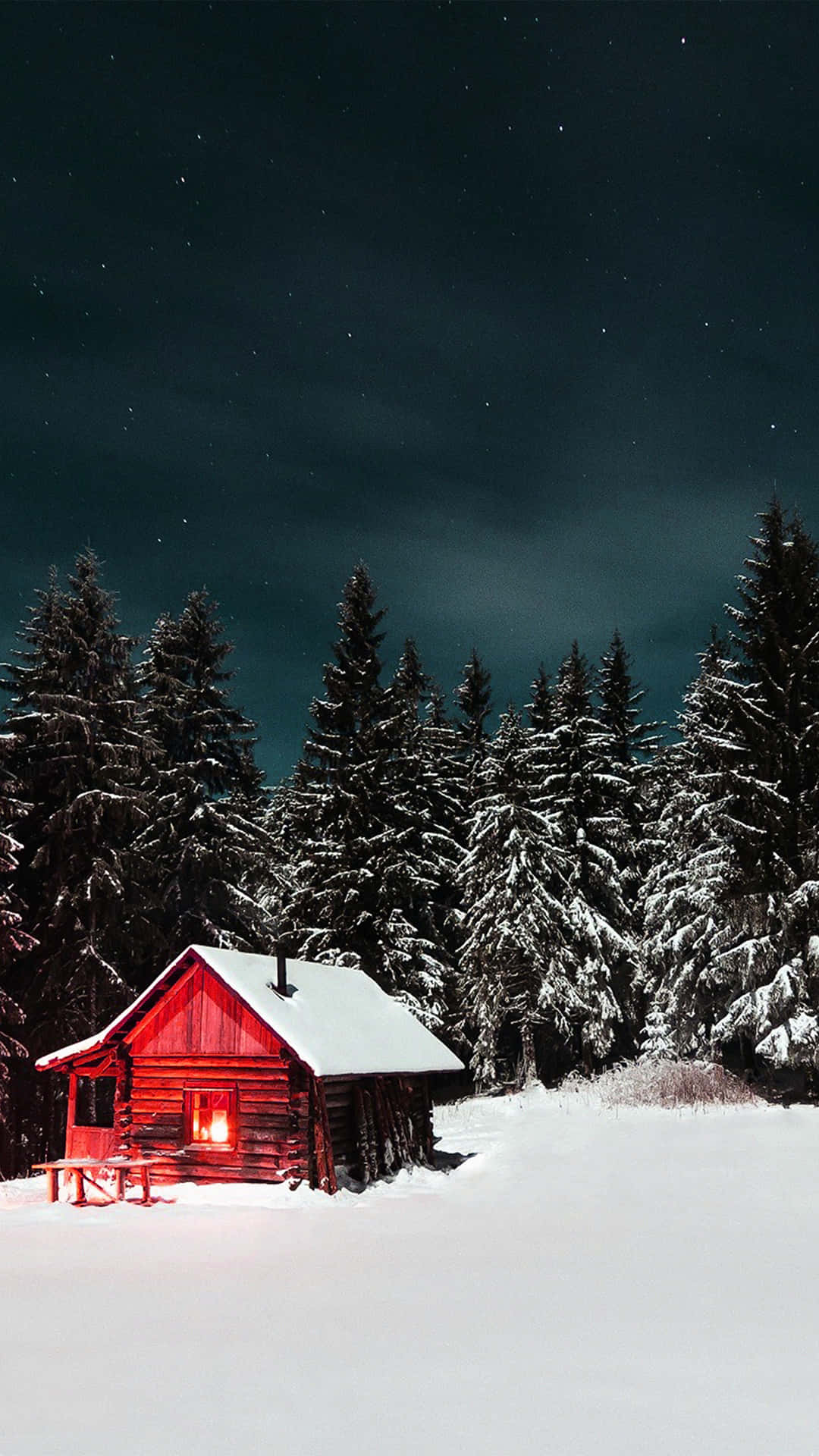 在繁星點點的夜空下，雪地森林中一間有亮著窗戶的紅色小屋。