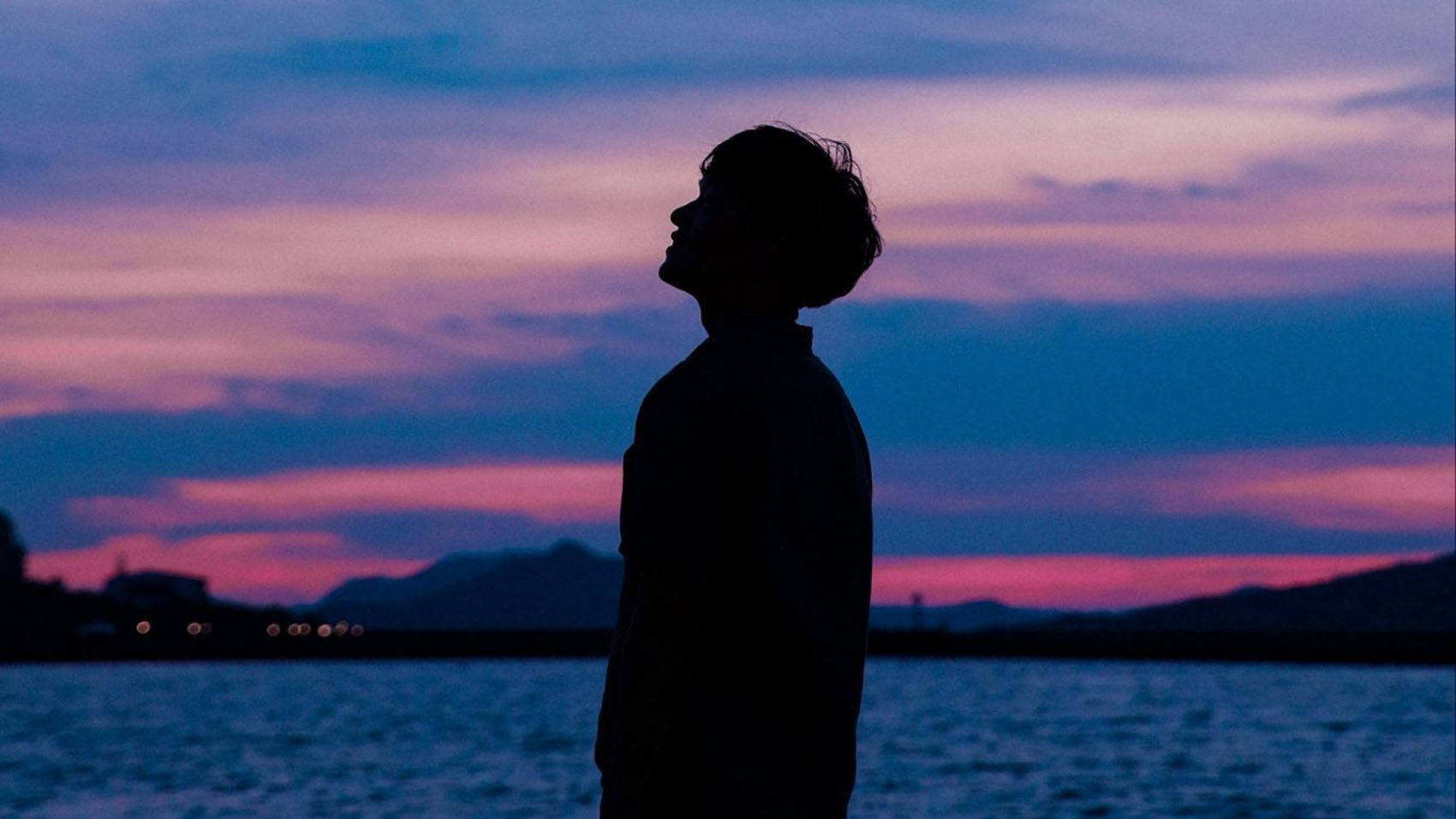 黃昏時分企喺水邊仰望色彩繽紛天空嘅人