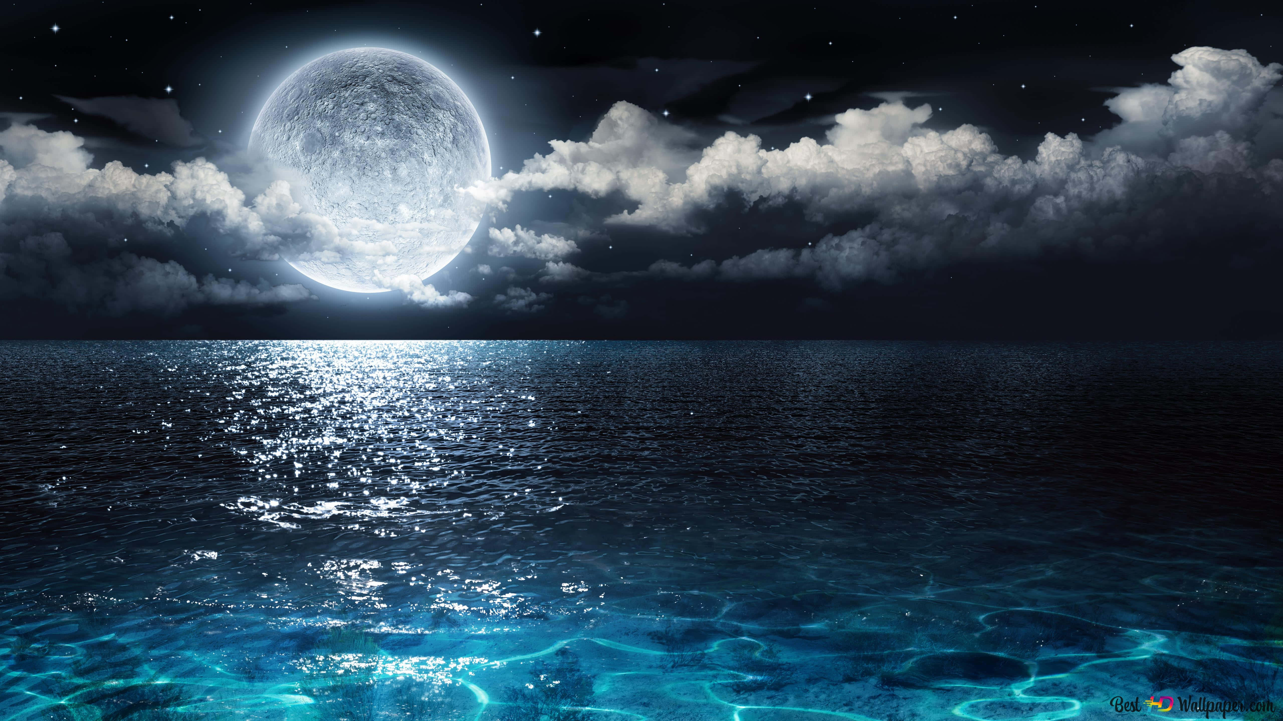 夢幻夜空 壁紙 — 一輪明亮的滿月在戲劇性的雲層後發光，照耀著星光夜空下波光粼粼的海洋。