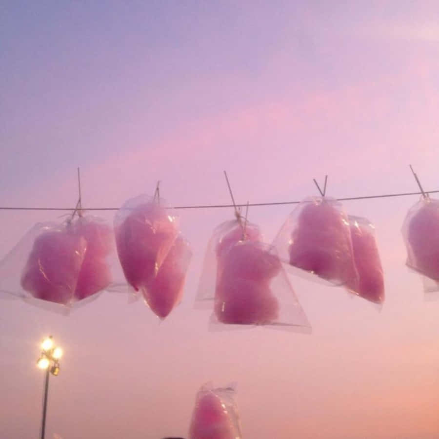 夢幻柔粉美學，提升你的心情 壁紙 — 粉紅色棉花糖袋掛在鐵線上，背景是柔和的紫色和粉紅色暮色天空，下方有路燈閃耀。