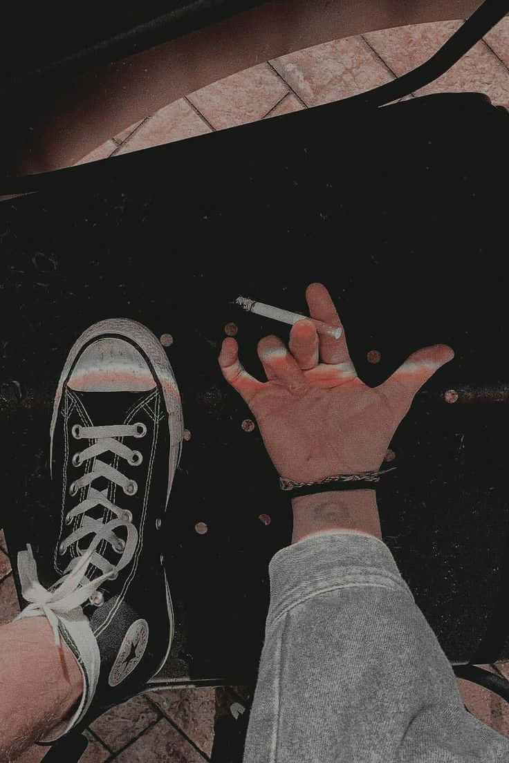手拎住煙喺黑色Converse運動鞋旁邊，深色表面。