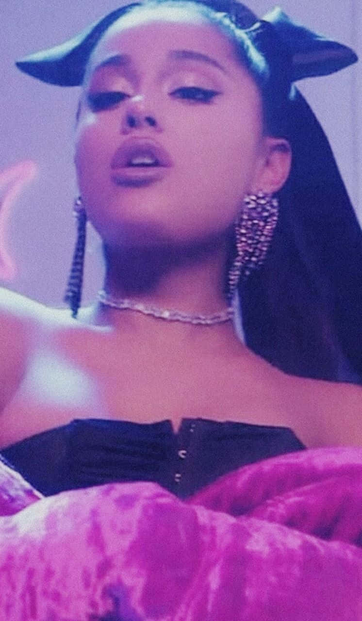 Ariana Grande 在紫色燈光環境中戴著貓耳和閃閃發光的珠寶。