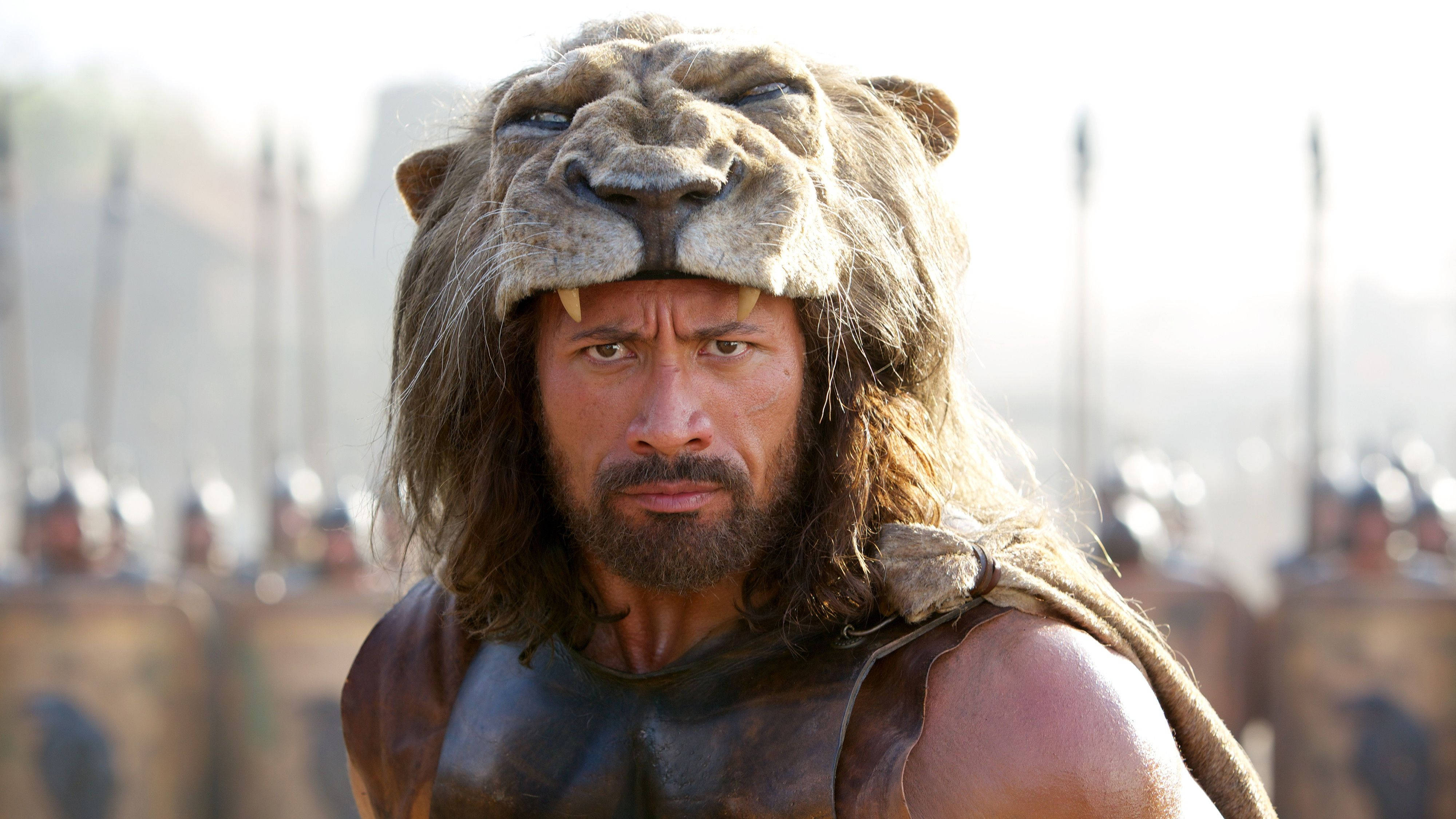 大力神戴獅頭冠冕 壁紙 — Dwayne Johnson 飾演嘅戰士戴住獅子頭盔，挑釁咁企喺模糊嘅士兵軍隊前面。