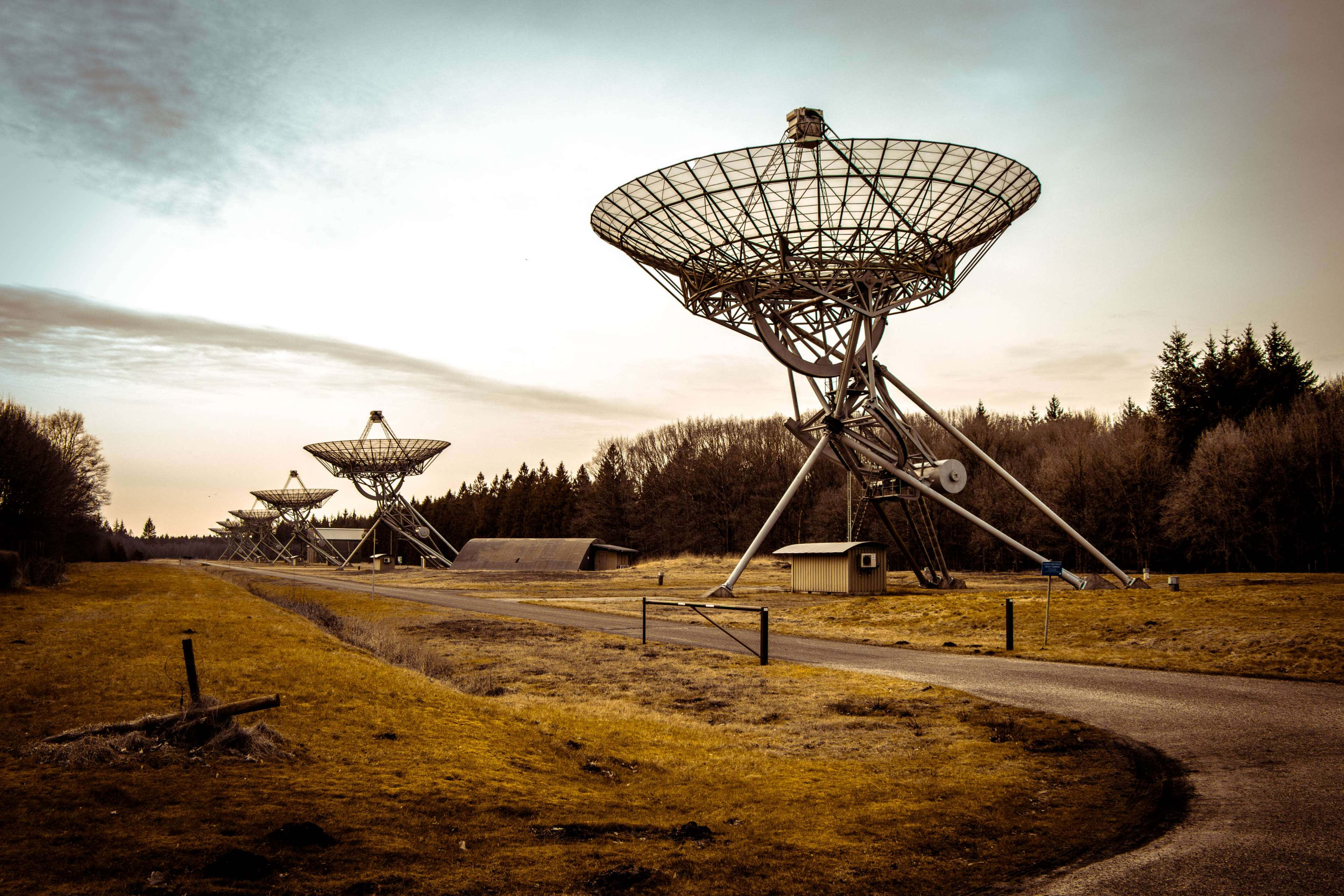 Radio Telescope 桌布 壁紙 — 大型無線電望遠鏡矗立在黃昏時的草地上，背景有樹木。