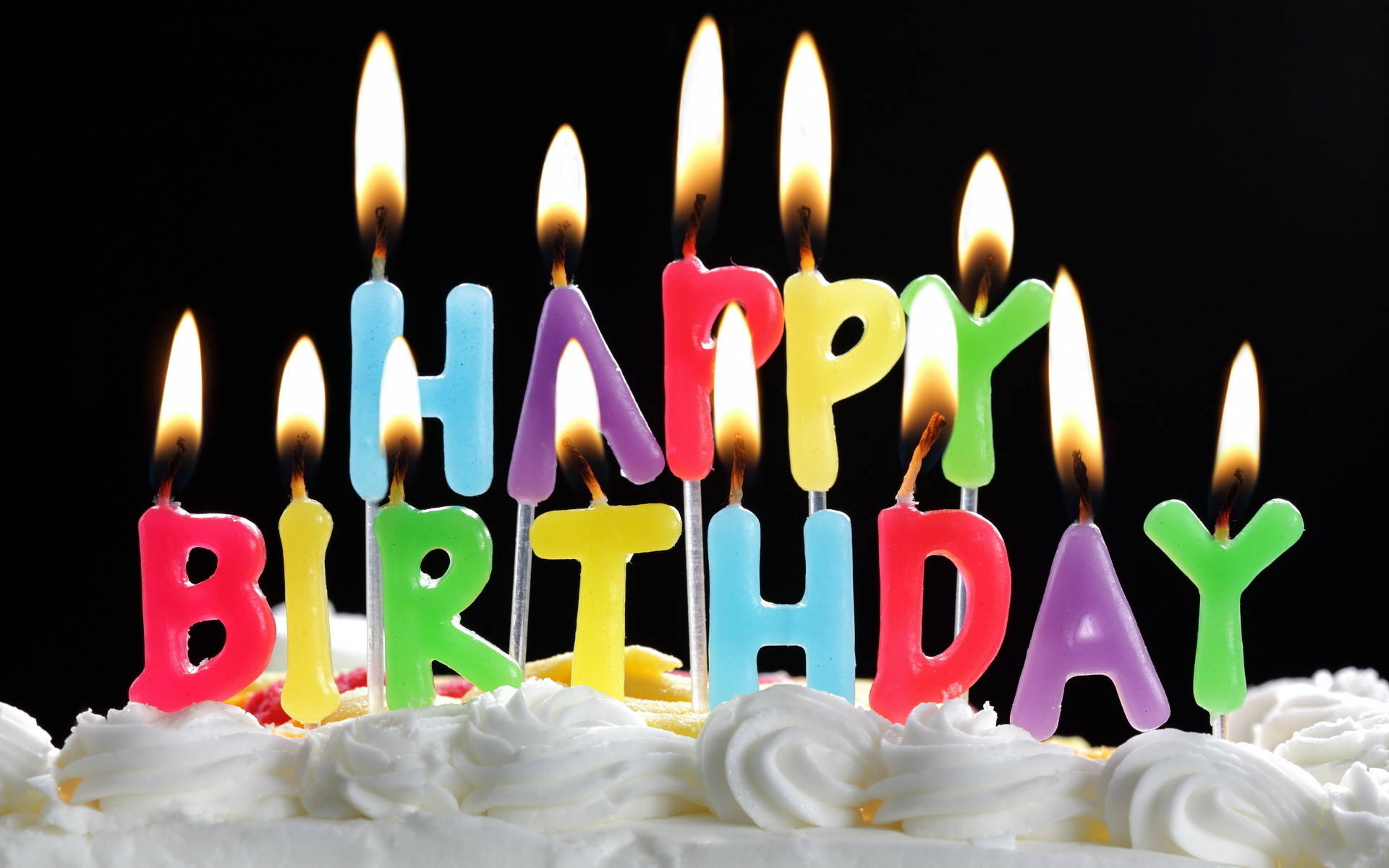 大尺寸彩色生日蛋糕蠟燭 壁紙 — 色彩繽紛的字母蠟燭拼出 happy birthday，在黑色背景的糖霜蛋糕上溫暖地發光。