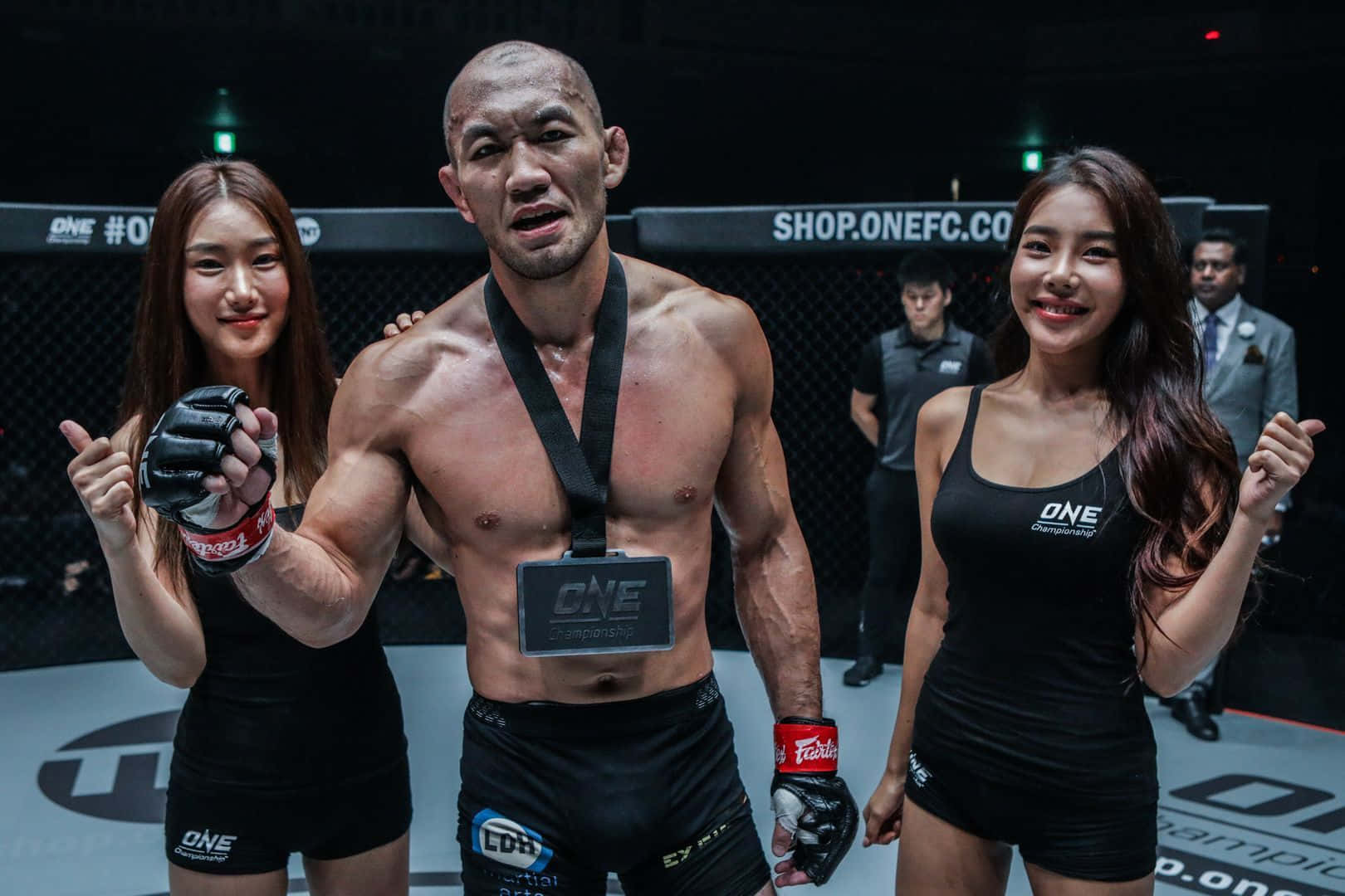 MMA拳手掛著冠軍獎牌，兩旁有兩位身穿黑色服裝的擂台女郎。