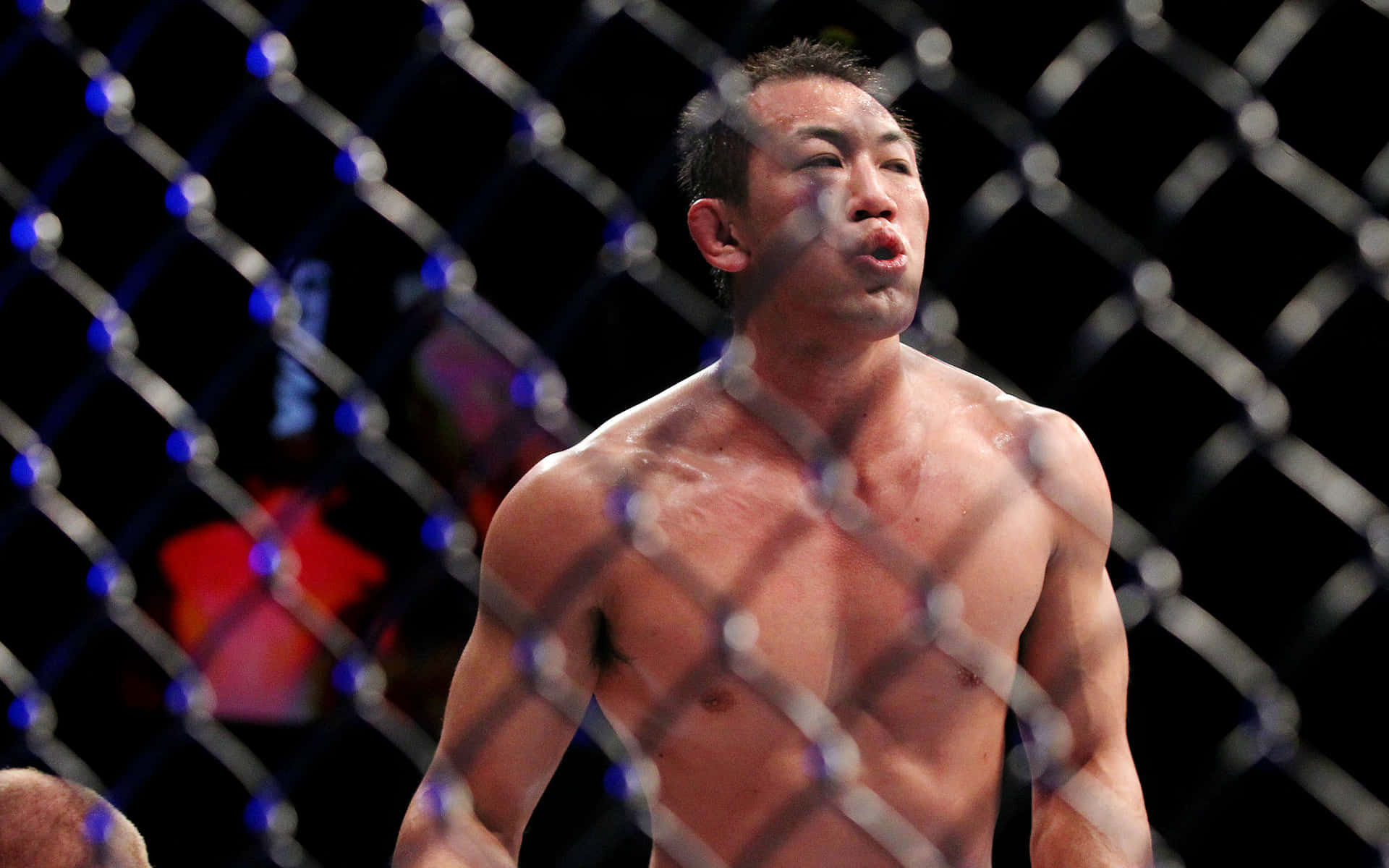 一名汗流浹背的MMA拳手在比賽中於籠內沉重地呼吸。