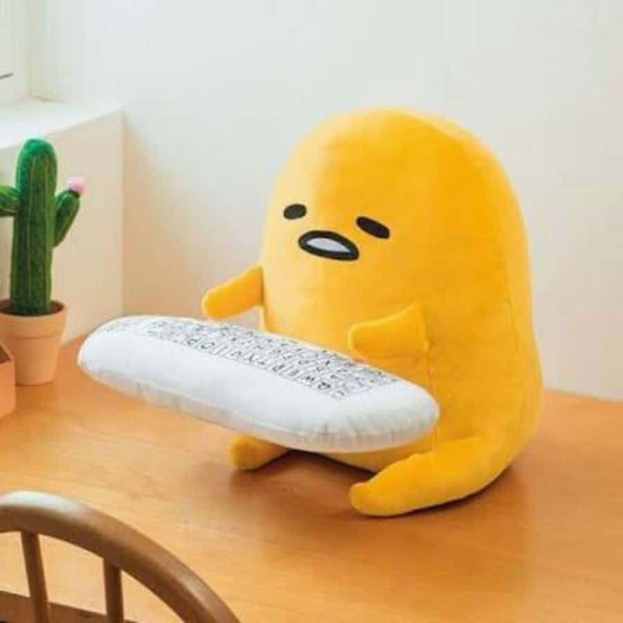 黃色 Gudetama 毛公仔喺木枱上攬住枕頭，旁邊有仙人掌。