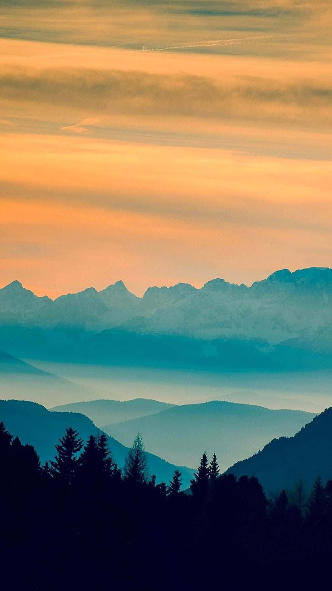 在充滿活力的橙色和藍綠色日落天空下，山脈輪廓映襯著大氣薄霧。
