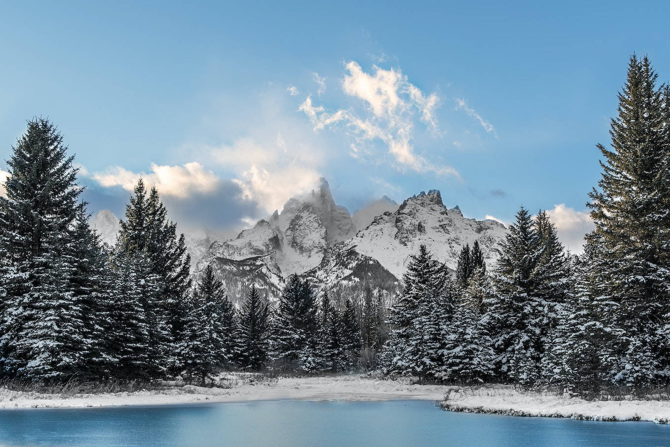 冬季冰凍湖泊和常綠樹木後方的雪山。