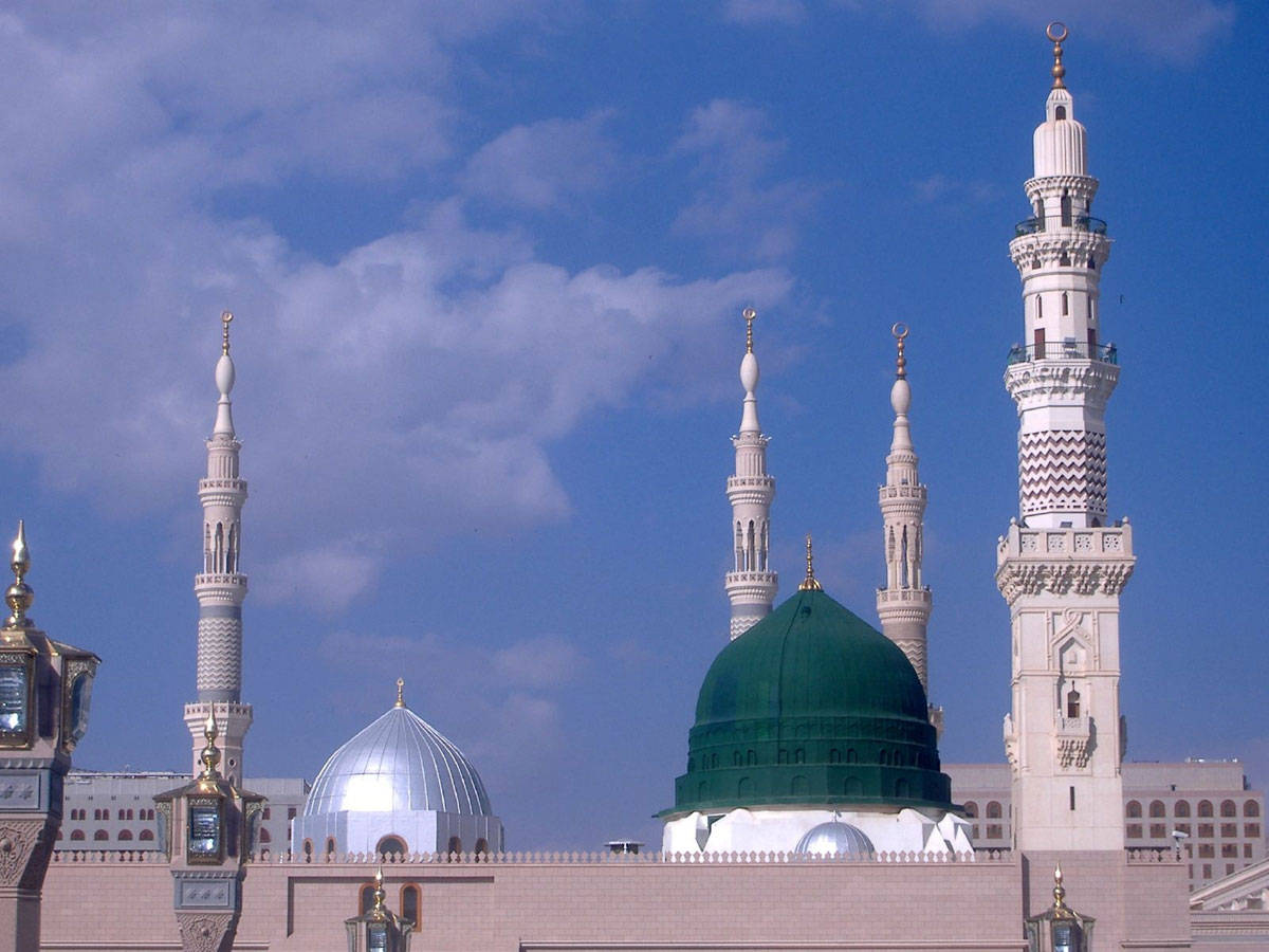 Madina Sharif 桌布 壁紙 — 大清真寺，擁有綠色和銀色圓頂及高聳宣禮塔，背景是明亮藍天和零星雲朵。