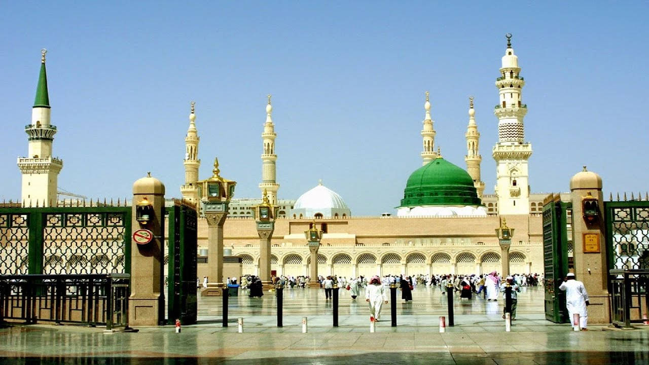 Madina Sharif 桌布 壁紙 — 大清真寺，綠色圓頂和宣禮塔，在晴朗的藍天下，朝聖者們在庭院中行走。