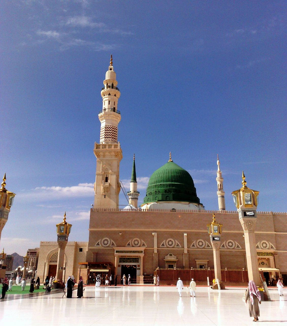 Madina Sharif 桌布 壁紙 — 大清真寺，綠色圓頂和高聳宣禮塔，在清澈藍天下，人們在反射廣場上行走。
