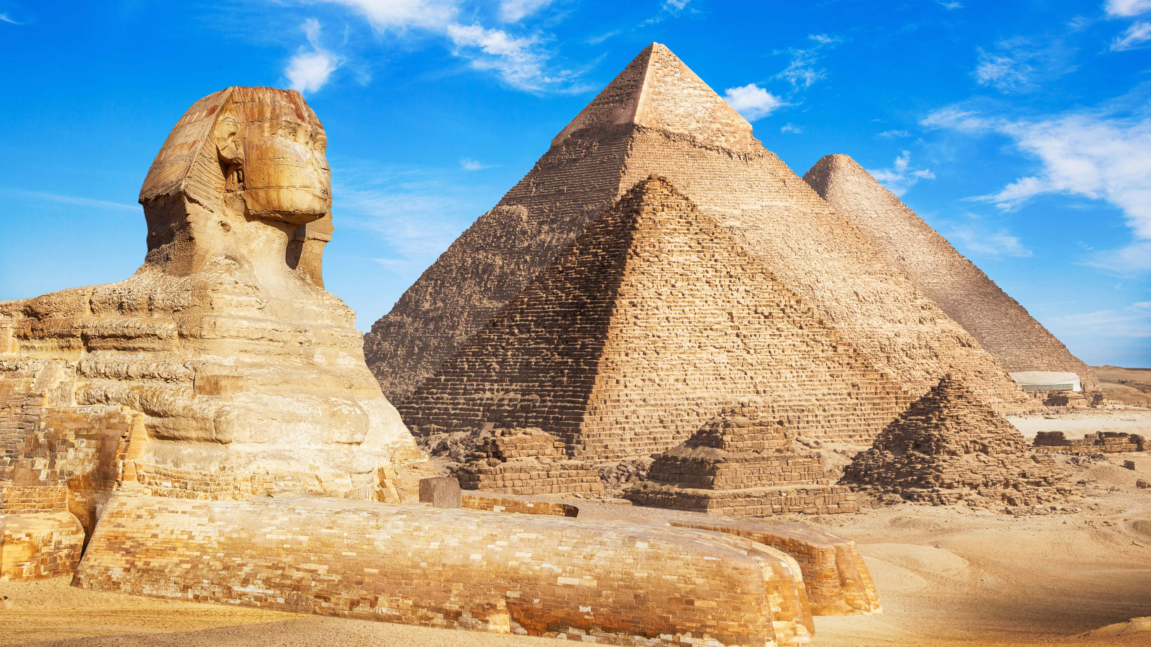 Ancient Egypt 桌布 壁紙 — 大獅身人面像和吉薩金字塔在明亮的藍天和散落的雲朵下雄偉地聳立。
