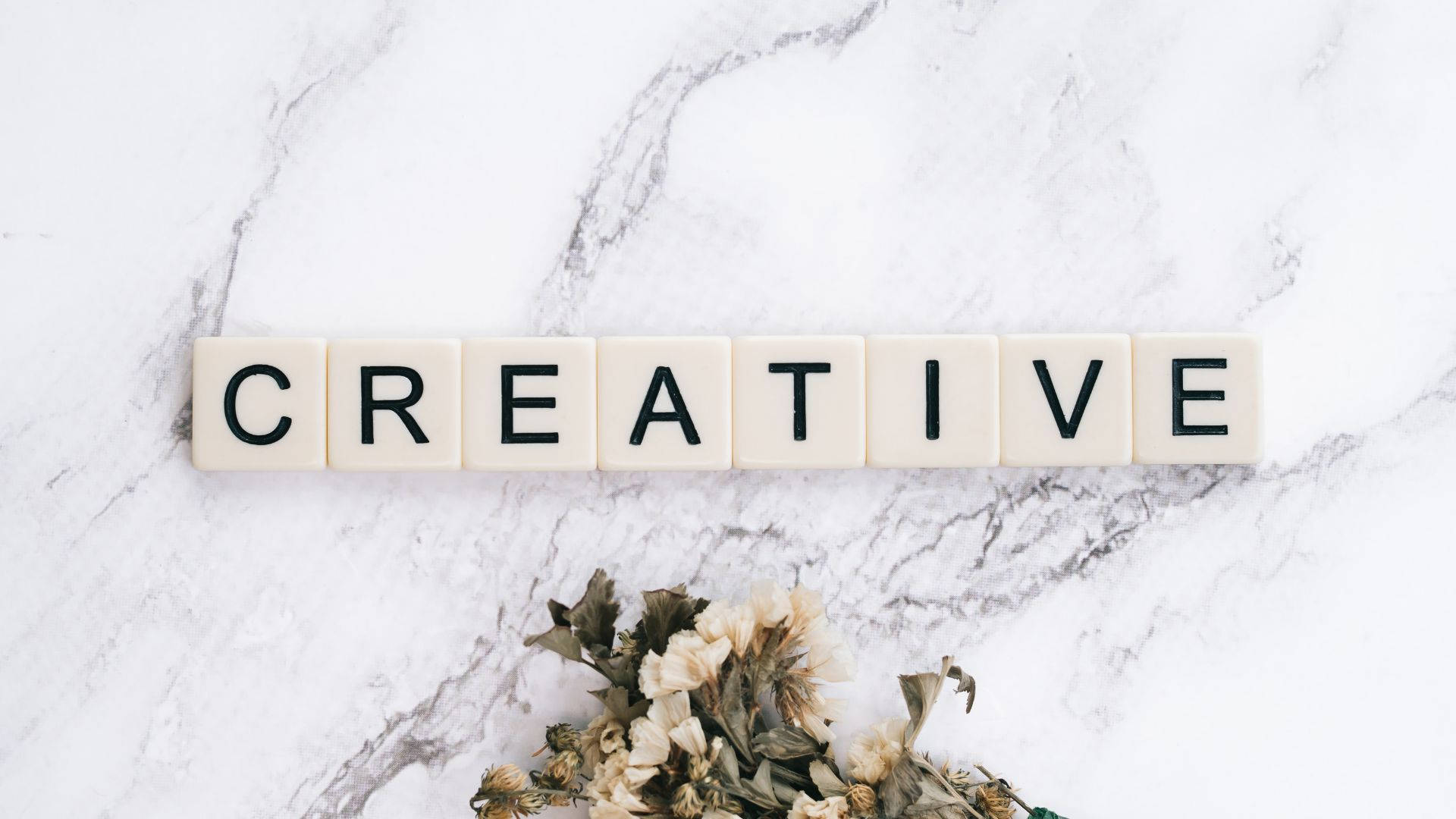 奶油色瓷磚在大理石上拼出creative，下方有乾花。