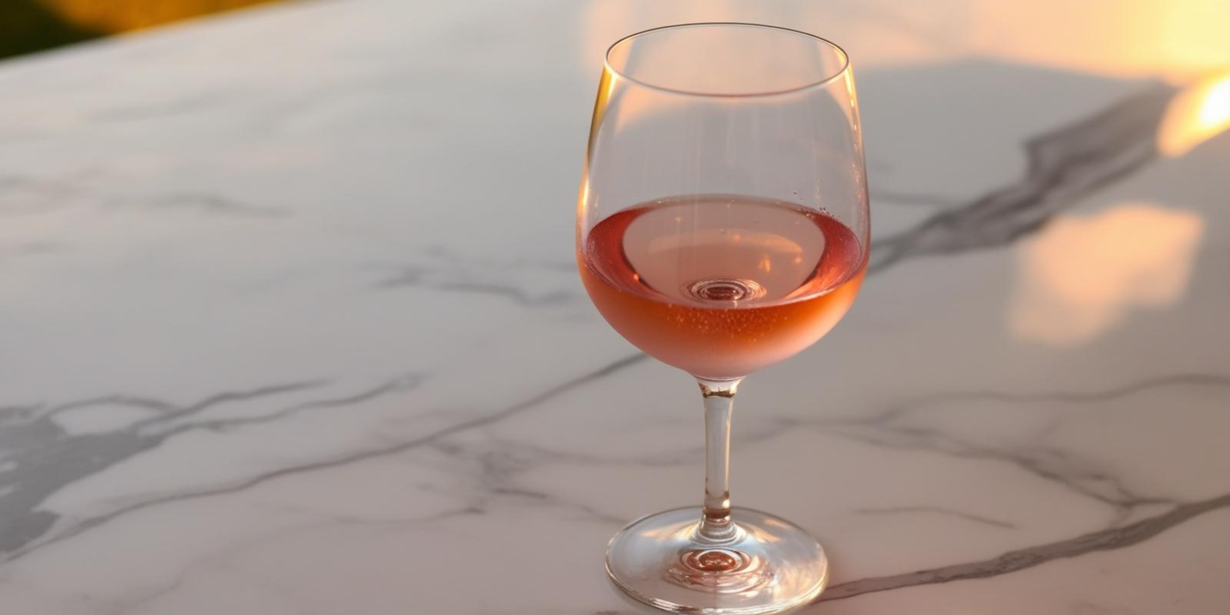 大理石桌上酒杯 壁紙 — 一杯玫瑰紅酒在日落時分在白色大理石表面上閃爍著金色光芒。