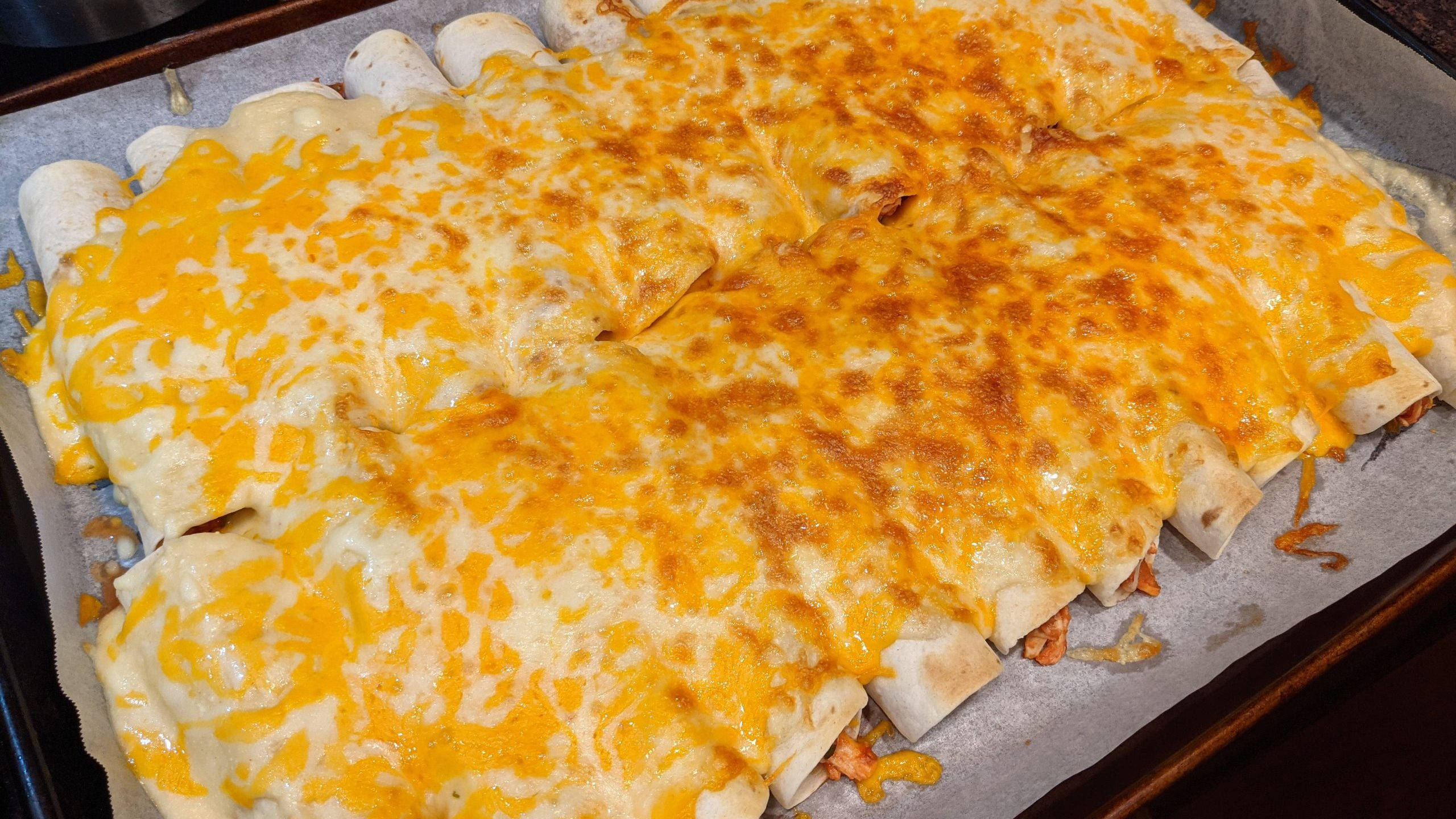 大盤豐盛奶酪 enchiladas 壁紙 — 金黃色的融化芝士覆蓋在鋪有烘焙紙的烤盤上新鮮出爐的捲餅上。