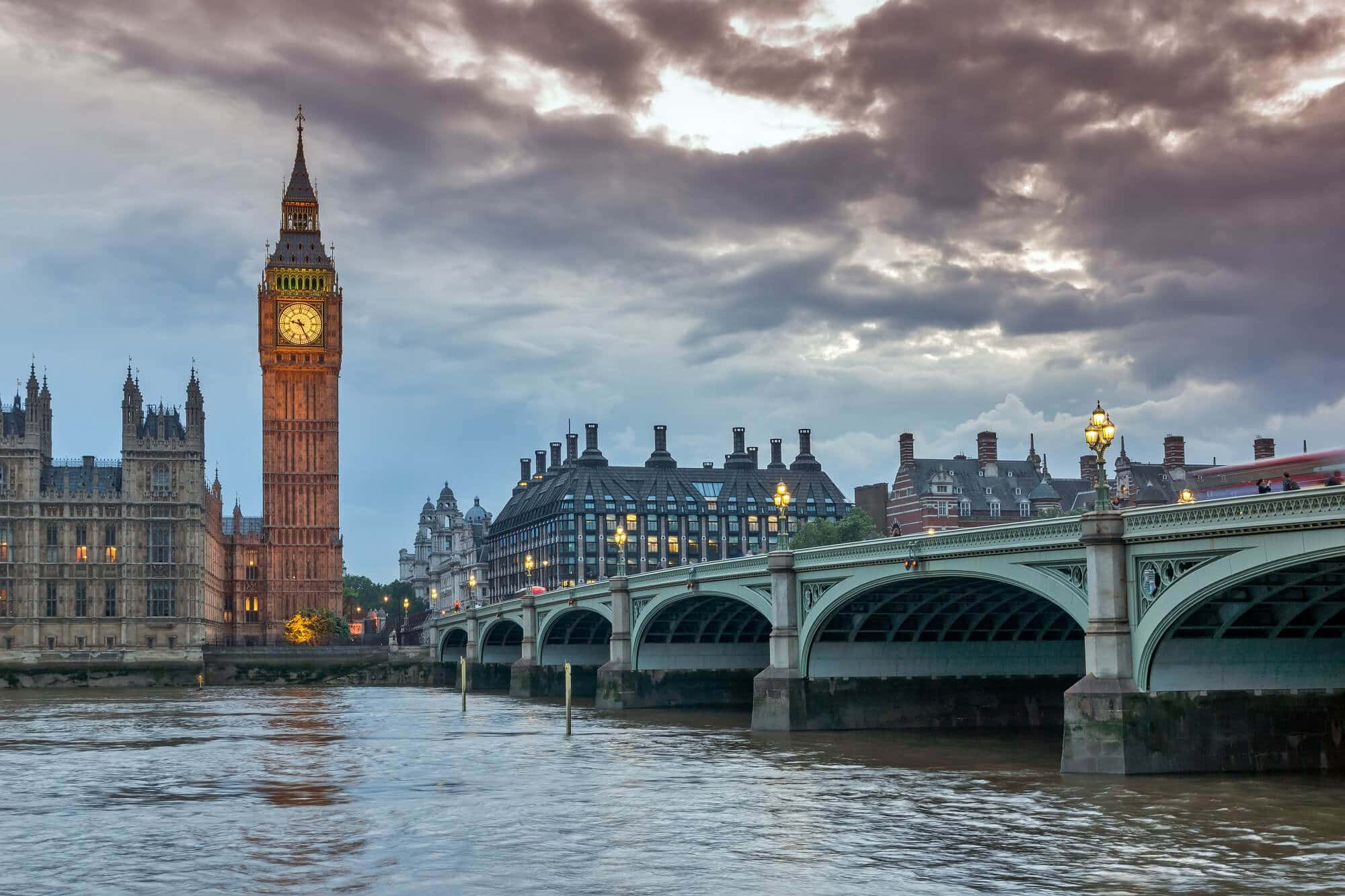UK 桌布 壁紙 — 大笨鐘和西敏橋在暮色雲層下閃耀，泰晤士河反射出它們溫暖的燈光。