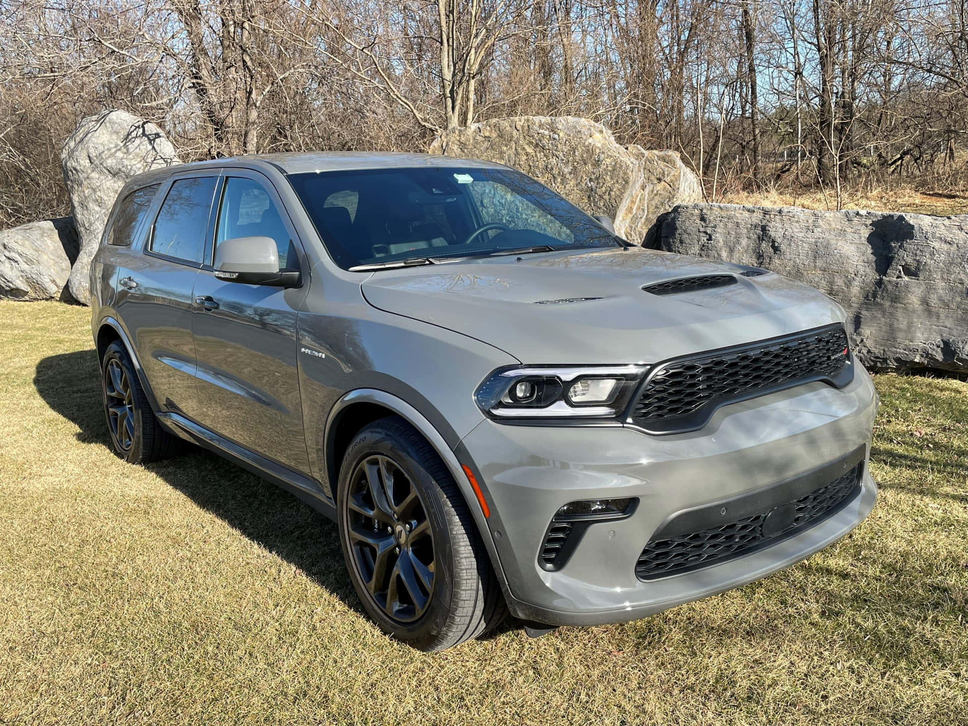 灰色 Dodge Durango SUV 停泊在戶外草地上，靠近大石頭和光禿禿的樹木。