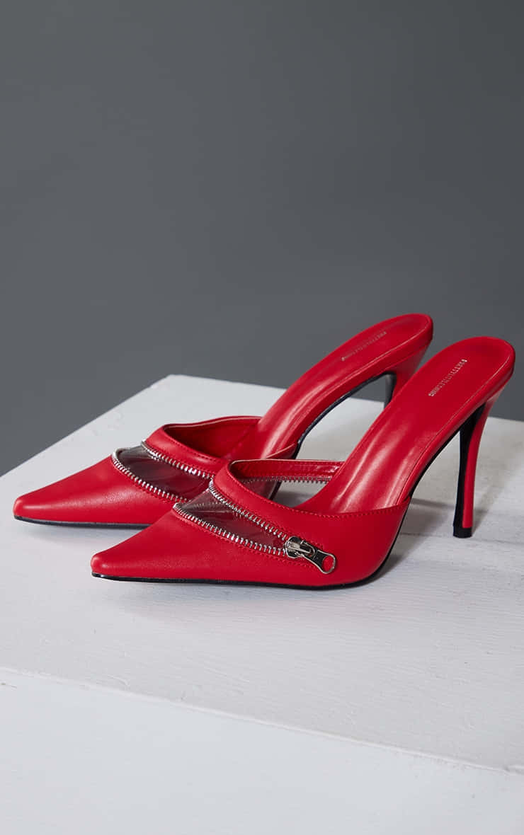 Red High Heels 桌布 壁紙 — 大膽的紅色高跟穆勒鞋搭配銀色拉鍊，優雅地放置在灰色背景下的白色木質表面上。