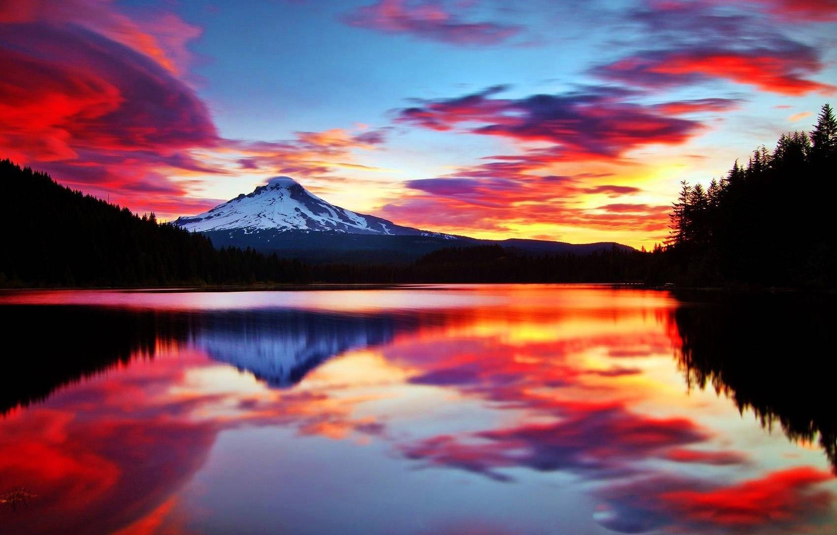 夕陽下積雪的山峰倒映在湖中，伴有火紅的雲彩。