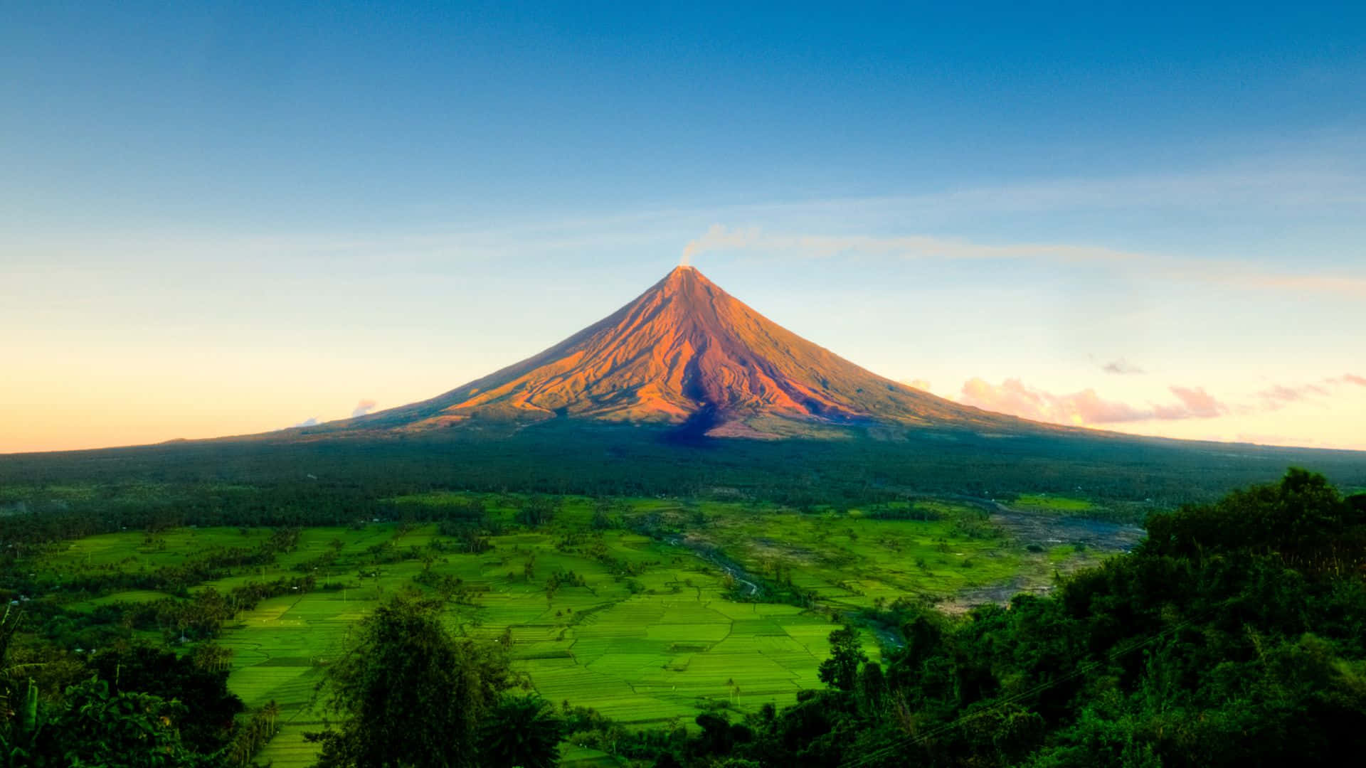 日出時分，火山與綠色稻田。