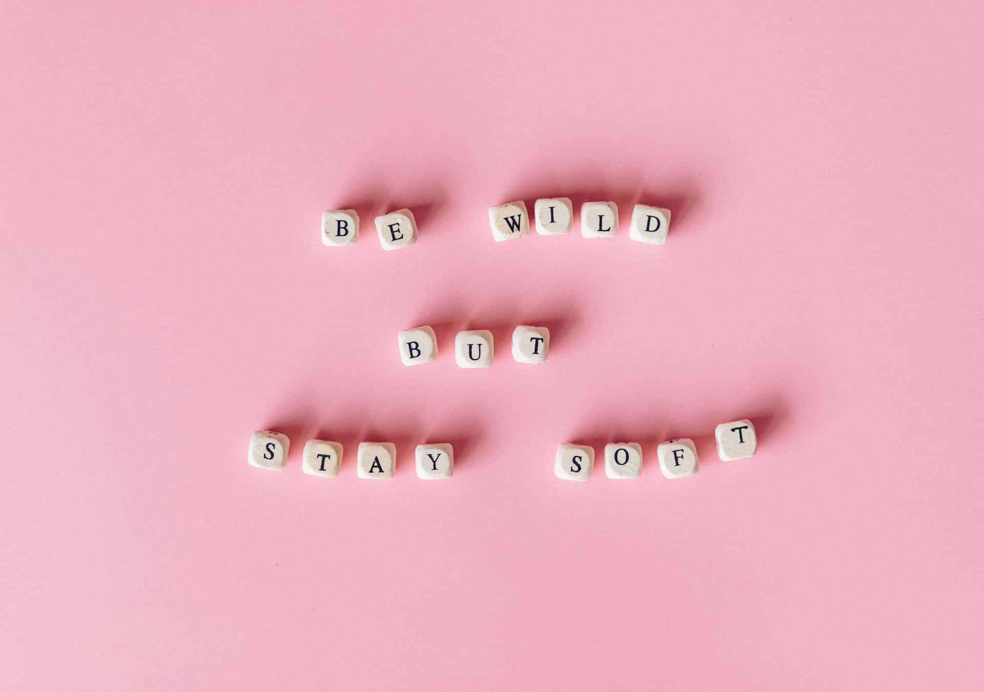 在粉紅色背景上拼出「Be Wild But Stay Soft」的白色字母方塊。