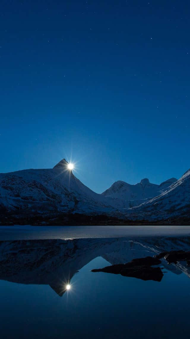 明亮月光下白雪覆蓋的山峰在夜間平靜的湖面上反射。