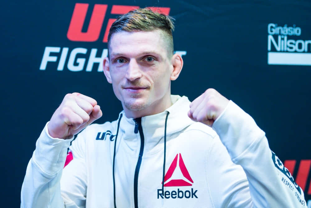 大衛·德沃拉克賽後黑眼圈 壁紙 — 一位堅定的UFC拳手身穿白色Reebok連帽衫，在品牌背景前握緊拳頭擺姿勢。
