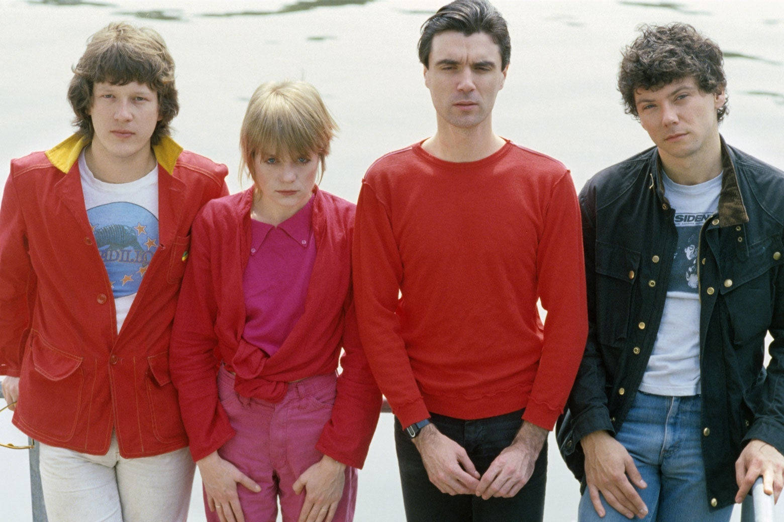 大衛·拜恩與 Talking Heads 重金屬樂隊 壁紙 — 四位身穿1970年代復古服裝的年輕男子，在模糊的水背景前莊嚴地站立。