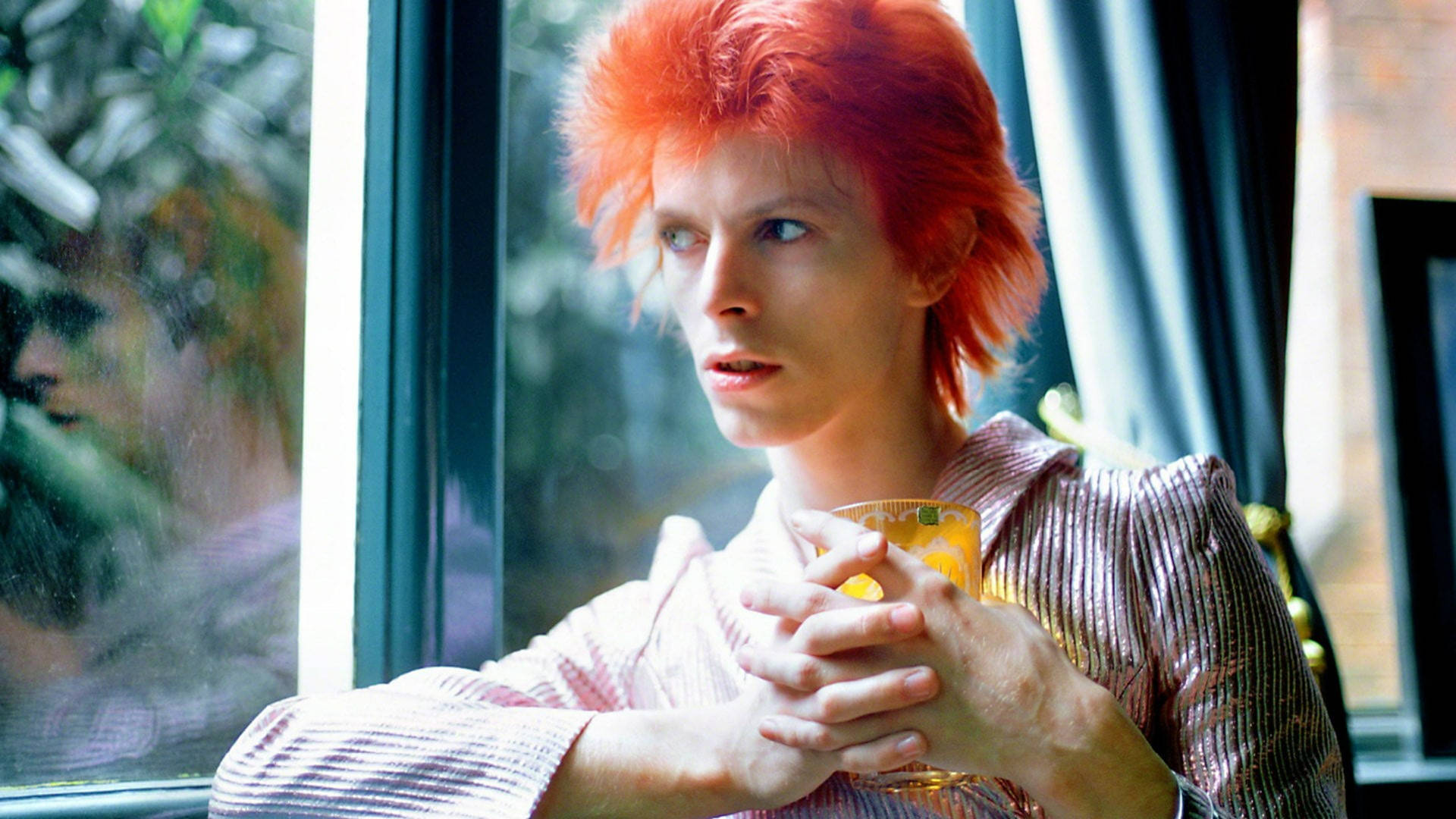 David Bowie 紅髮在窗邊拿著飲品。