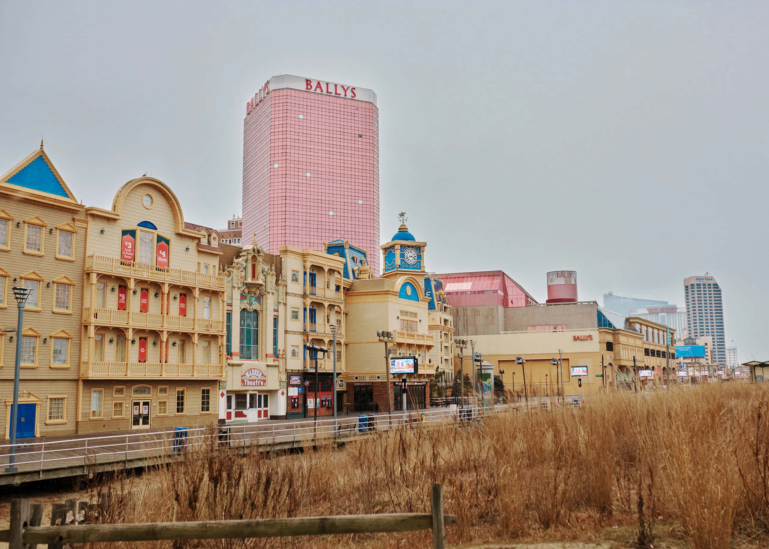 大西洋城可愛建築 壁紙 — 粉紅色的Bally's賭場塔樓在華麗的黃色建築後面升起，沿著水邊，前景有乾燥的蘆葦。