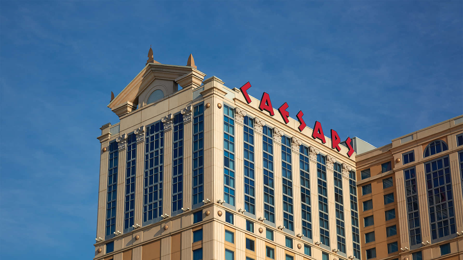 大西洋城海濱步道夜間璀璨燈光 壁紙 — Grand Caesar's Palace 酒店塔樓在清澈藍天下，配有醒目的紅色標誌和反光玻璃窗。