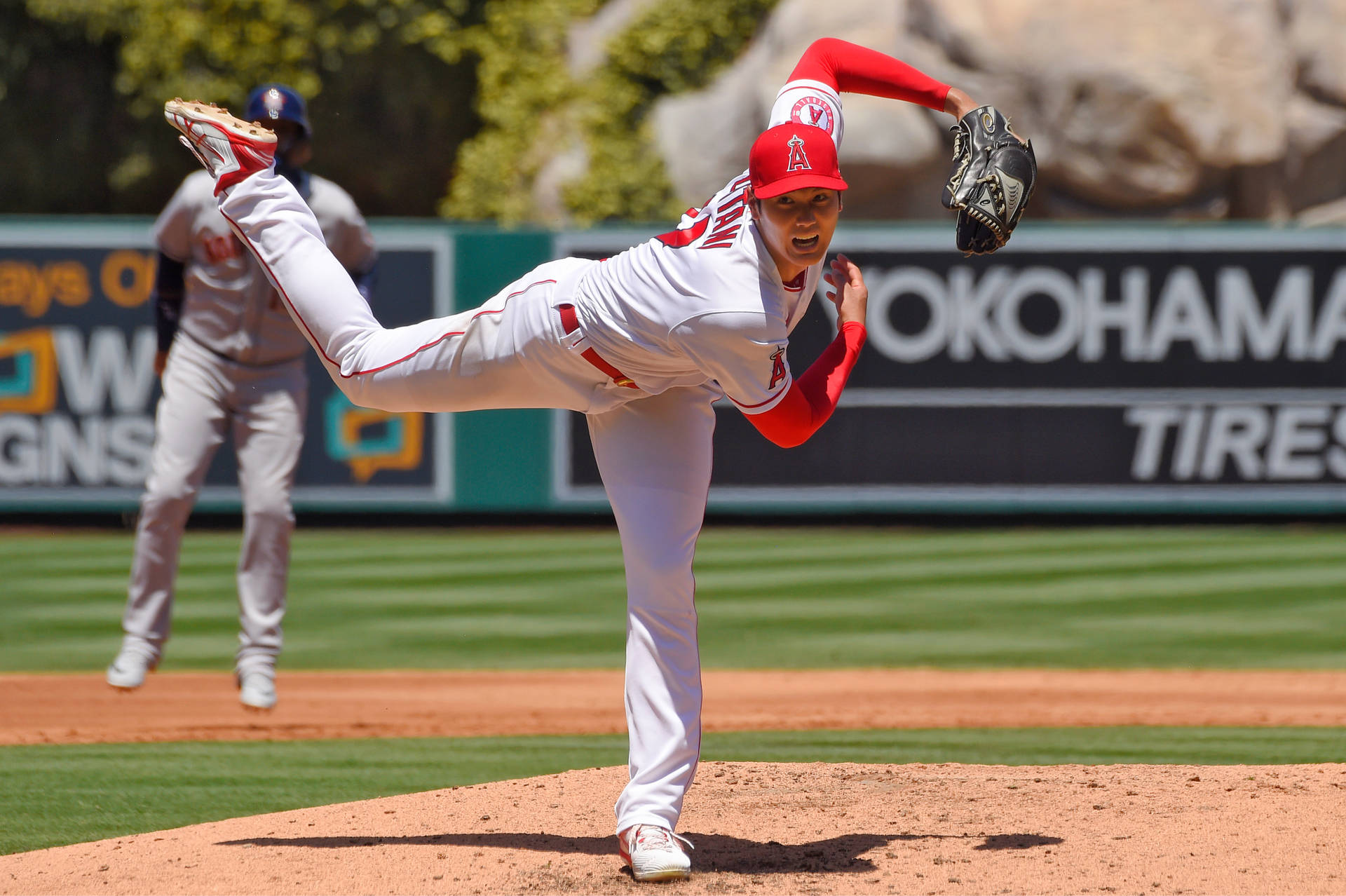 大谷翔平投球動作 壁紙 — 一位身穿白色和紅色制服嘅棒球投手，喺陽光普照嘅投手丘上專注地投球。