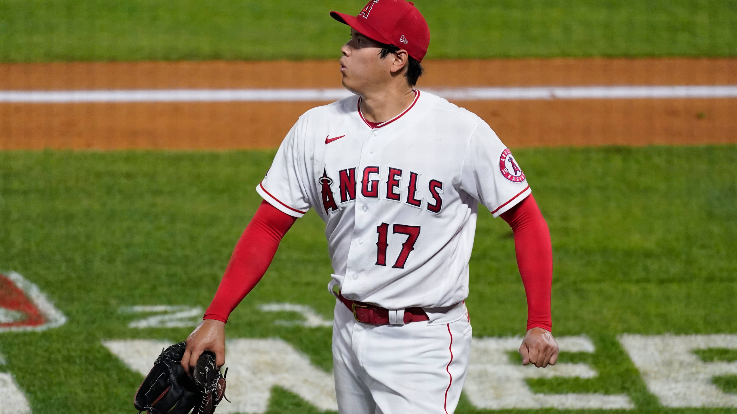 大谷翔平比賽中吐氣瞬間 壁紙 — 一名身穿白色天使隊球衣、背號17的棒球選手，戴著手套走過綠色球場。
